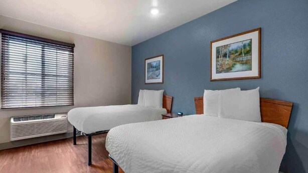 Quarto de hotel com duas camas, uma janela com persianas, um quadro na parede e um aquecedor sob a janela.