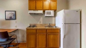 Cozinha compacta com armários de madeira, micro-ondas, geladeira, pia e uma cadeira.