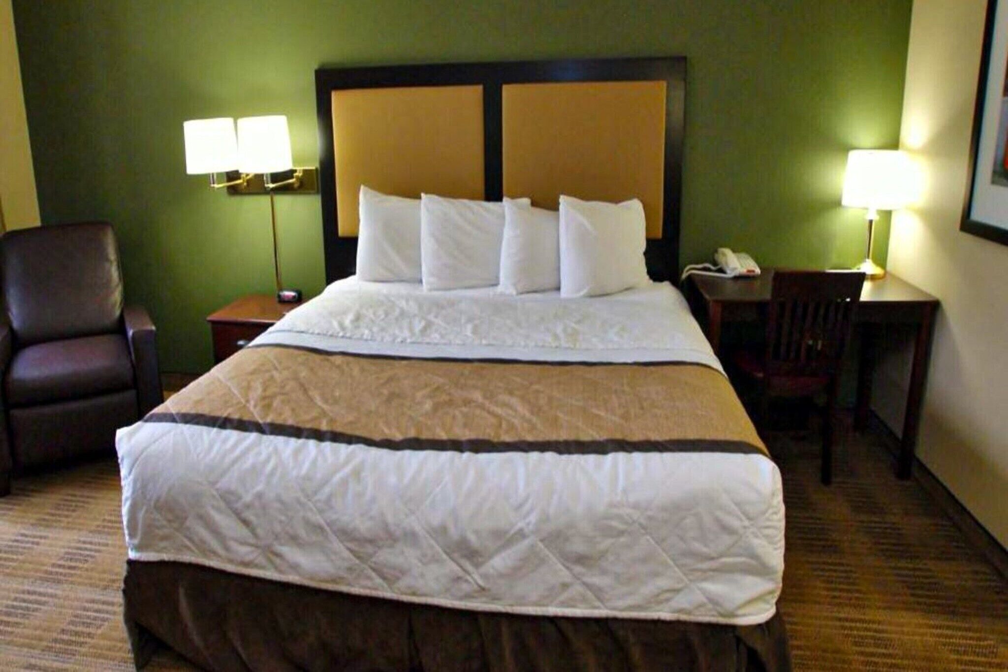 Une chambre d’hôtel avec un lit, une chaise, un bureau et deux lampes.