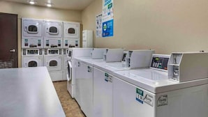 A laundry facility with multiple washing machines and dryers, a control panel, and informational posters on the wall.
