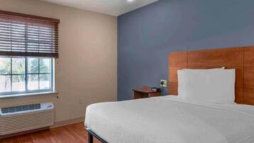 A hotel room with a bed, a window with blinds, a heater, and a nightstand.