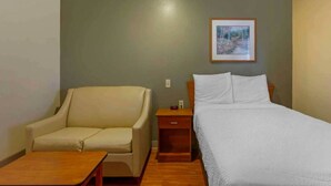 A room with a bed, a chair, a small table, a nightstand, and a framed picture on the wall. - 1 Bed | Deluxe, Sofa-Bed (Bossier City)