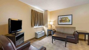 Ein Hotelzimmer mit Flachbildfernseher, einer Couch, einem Couchtisch, einem Beistelltisch mit Lampe und einem gerahmten Bild an der Wand.