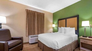 A hotel room with a bed, a chair, a lamp, and a heater.