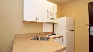 A compact kitchen with white cabinets, a microwave, a refrigerator, and a sink.