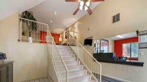 A hotel lobby with a staircase, reception desk, and a ceiling fan.