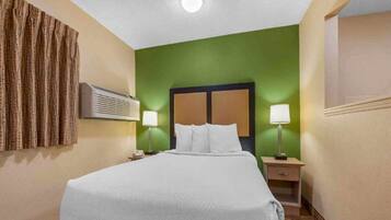 Habitación de hotel con cama, mesitas de noche, lámparas, equipo de aire acondicionado y una pared de acento verde.
