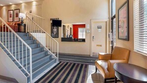 Eine Hotelhalle mit Treppe, einer Rezeption, einem Wartebereich und einem Fenster mit Jalousien.