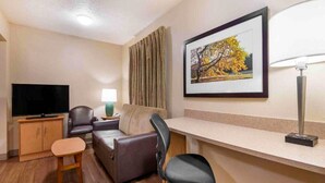 Ein Hotelzimmer mit Flachbildfernseher, Sofa, Schreibtisch, Stuhl, Lampe und einem gerahmten Bild an der Wand.