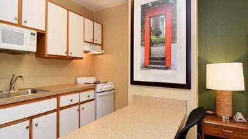 A compact kitchen with white cabinets, a microwave, a stove, a sink, and a framed picture on the wall.