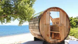Une structure en forme de tonneau, faite de bois et dotée d’une porte, située sur une terrasse en bois, près d’une plage.