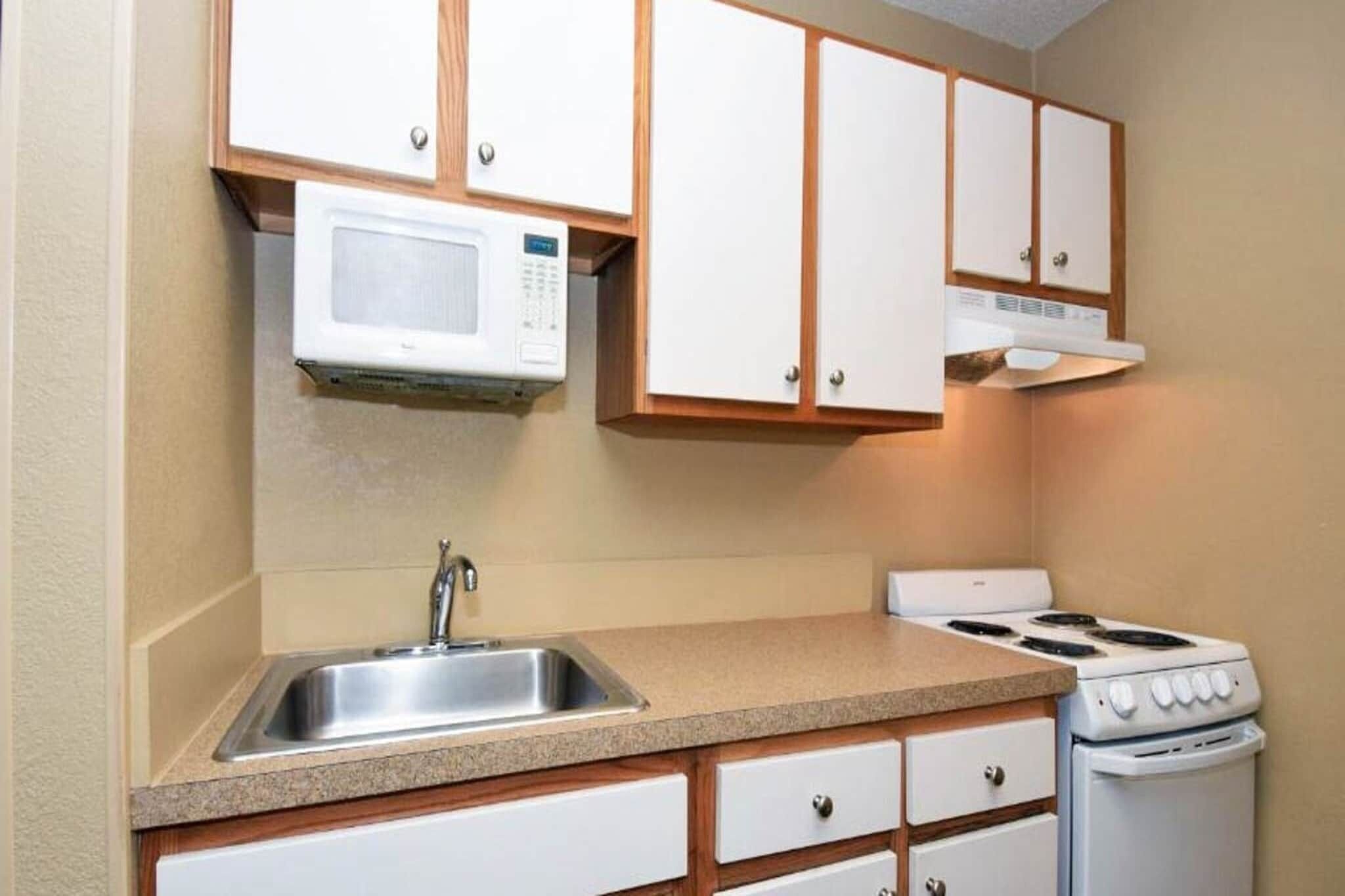 A compact kitchen with a microwave, stove, sink, and wooden cabinets.
