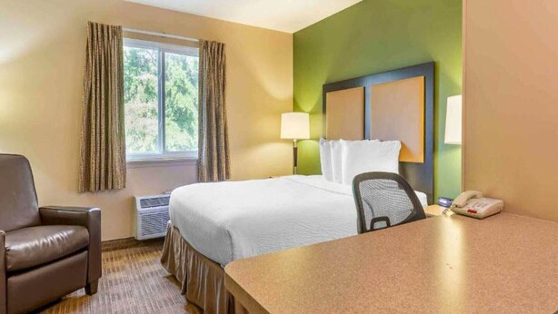 Ein Hotelzimmer mit Bett, Schreibtisch, Stuhl, Lampe und Telefon.