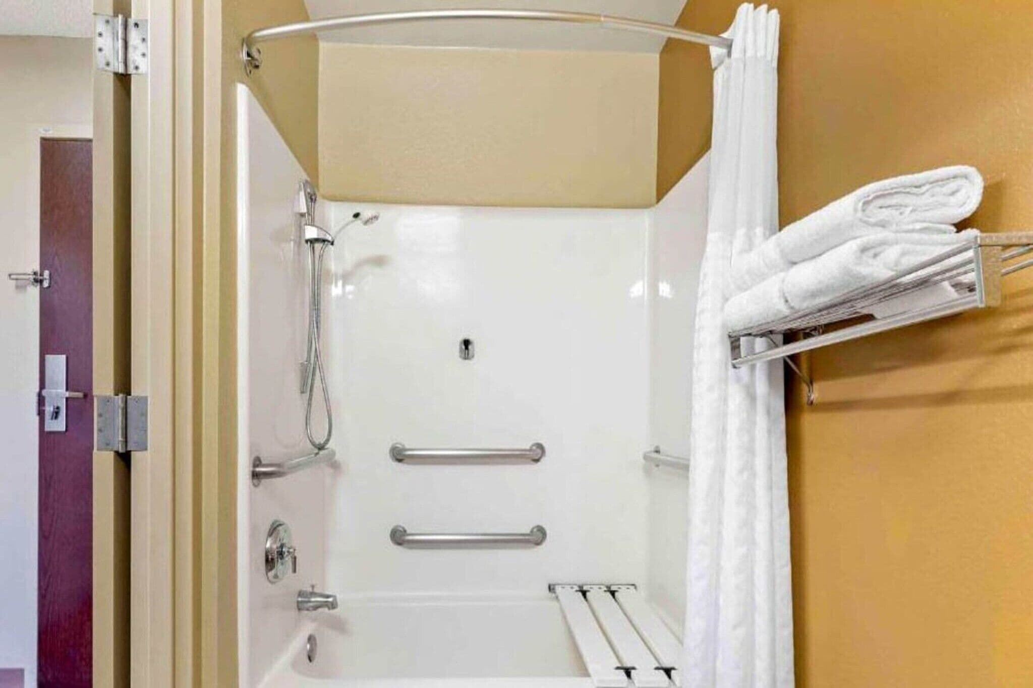 Eine Dusche mit Glastür, ein Handtuchhalter mit gefalteten Handtüchern und eine Metall-Haltestange.