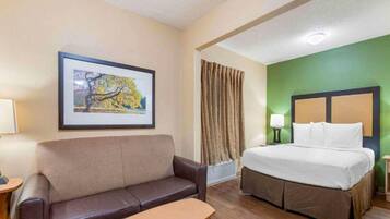 A hotel room with a bed, a couch, a small table, a framed picture on the wall, and a window with curtains.