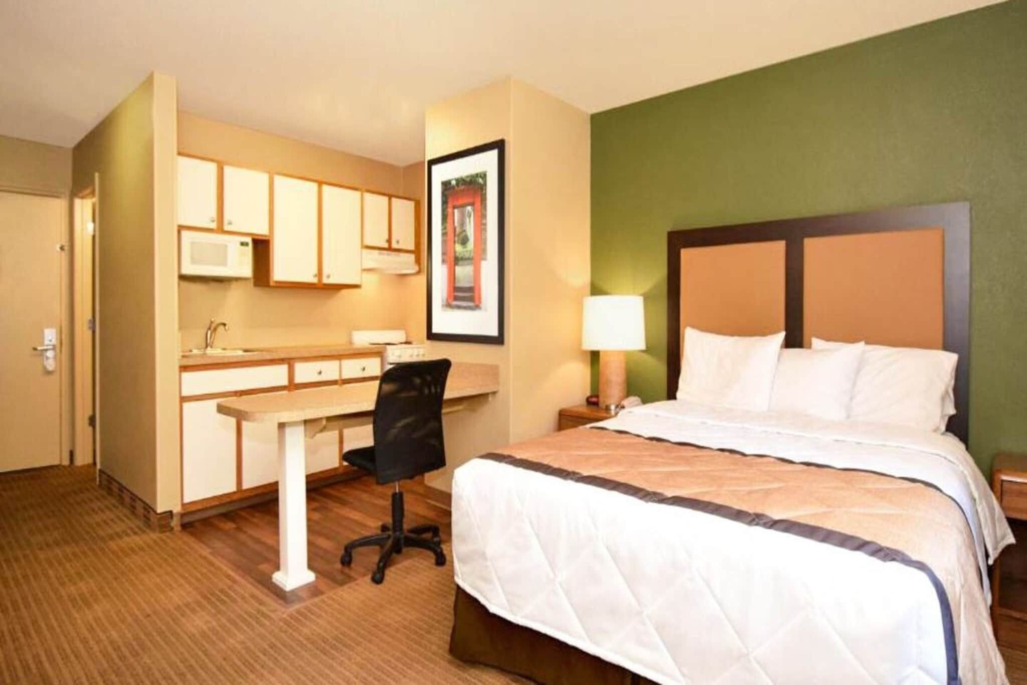 Habitación de hotel con cama, escritorio con silla, microondas y un cuadro en la pared.