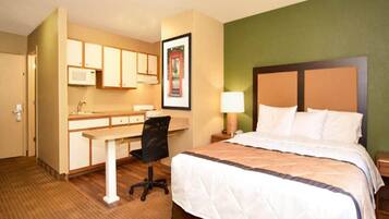 Habitación de hotel con cama, escritorio con silla, microondas y un cuadro en la pared.