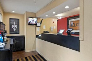 A reception area with a counter, a television mounted on the wall, a framed trophy, and a welcome sign.