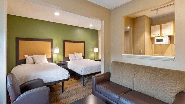 Une chambre d’hôtel avec deux lits, un canapé, une petite table et un miroir.