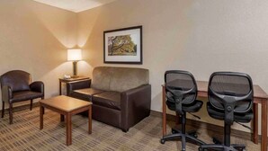 Une chambre d’hôtel avec un canapé, deux fauteuils, une petite table, une lampe et un tableau encadré au mur.
