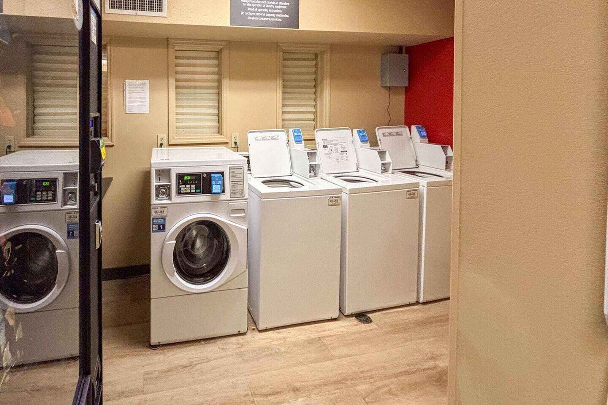 A laundry facility with multiple washing machines and dryers, a wooden floor, and a red accent wall.