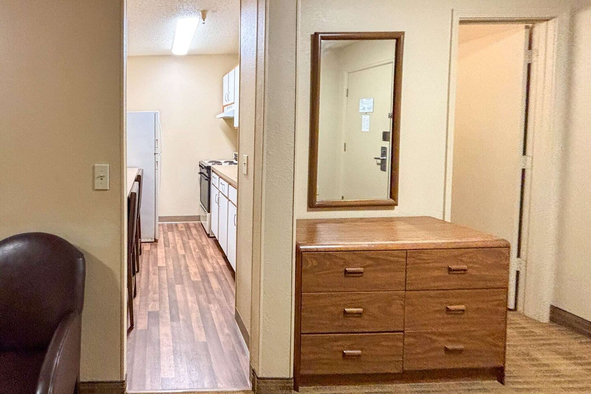 Een gang met een houten dressoir, een spiegel, een deur en een koelkast op de achtergrond.