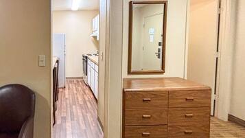 Een gang met een houten dressoir, een spiegel, een deur en een koelkast op de achtergrond.