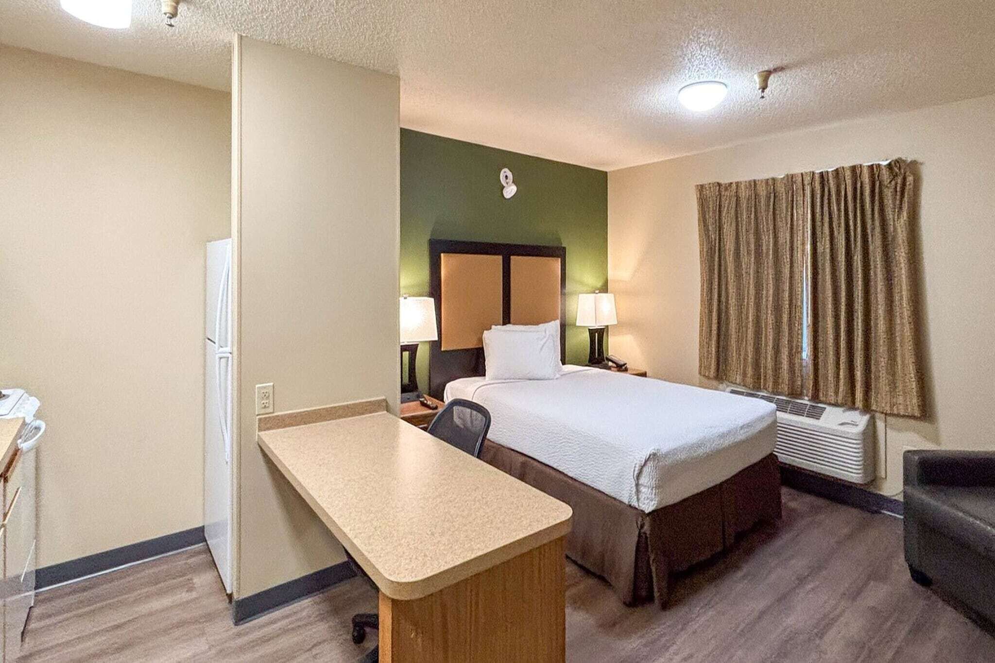 A hotel room with a bed, desk, chair, and a window with curtains.