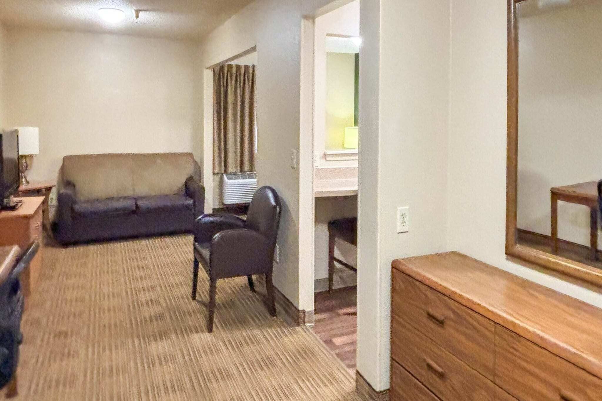 Une pièce comprenant un canapé, un fauteuil, une commode en bois et un miroir.