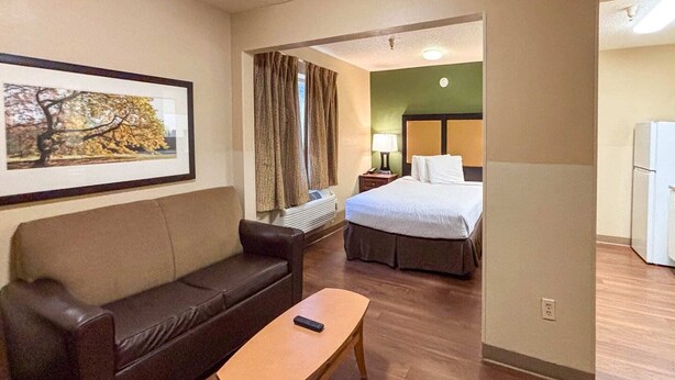Een hotelkamer met een bed, een bank, een kleine tafel, een lamp en een koelkast.
