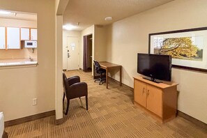 A hotel room with a kitchenette, a desk, a chair, a television, and a framed picture on the wall.