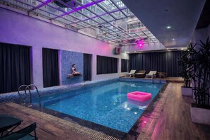 An indoor swimming pool with a glass ceiling, a person meditating on a ledge, and lounge chairs. - The Golden View Farm & Resort (Sonkach)