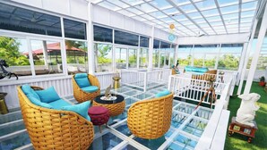 A covered patio with wicker furniture, a glass floor, and a white railing. - The Golden View Farm & Resort (Sonkach)