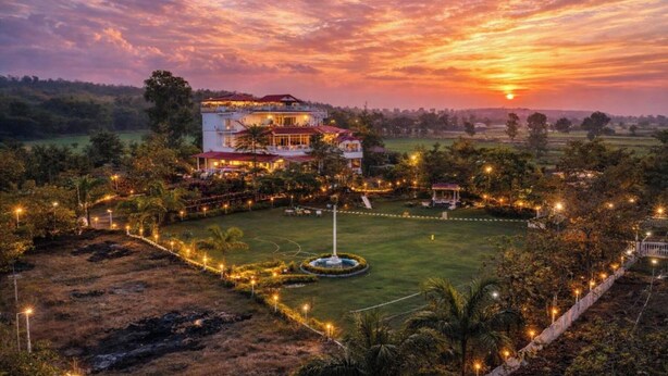 A large, multi-story building with a well-maintained lawn and a central fountain, surrounded by trees and pathways. - The Golden View Farm & Resort (Sonkach)