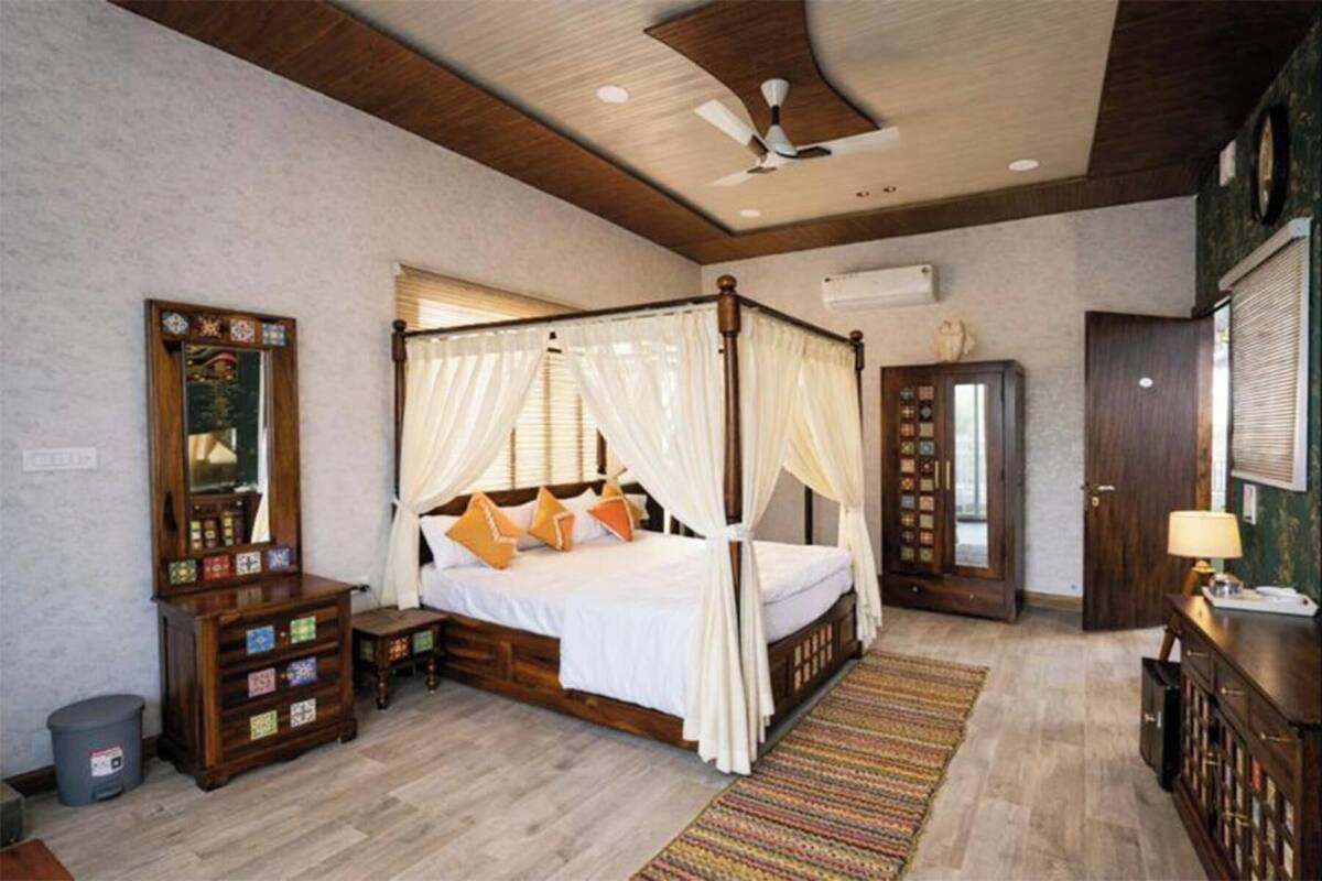 Un lit à baldaquin, une armoire en bois ornée de motifs décoratifs, un ventilateur de plafond et un grand miroir.