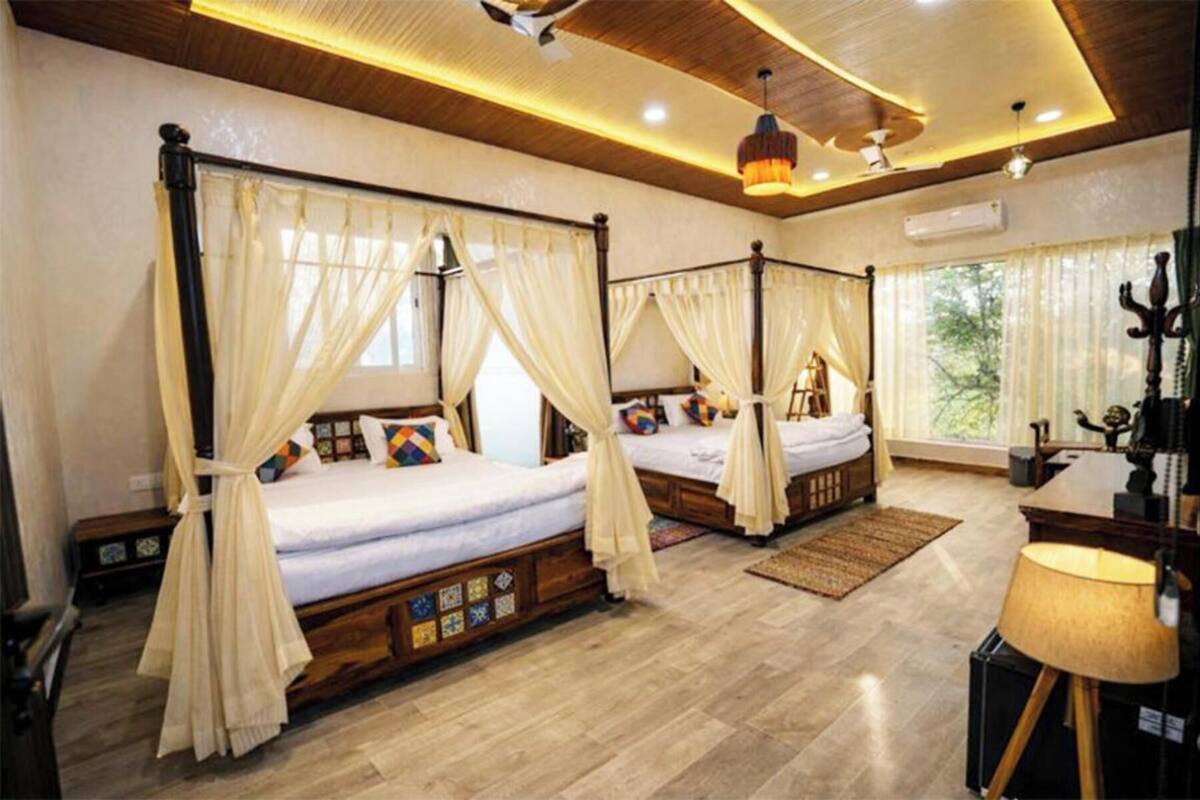 Une chambre dotée de deux lits à baldaquin, d’un plancher en bois, d’un bureau avec une lampe et d’une fenêtre avec des rideaux.