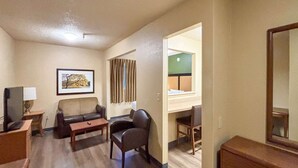 A hotel room with a sofa, a chair, a small table, a desk, a mirror, and a framed picture on the wall. - 1 Queen Bed | Non-Smoking, Micfridge, Sofa-Bed (Greenville SC)