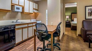 A compact hotel room with a kitchenette, a dining area with two chairs, a bed, a nightstand, and a lamp. - 1 Queen Bed | Non-Smoking, Micfridge, Sofa-Bed (Greenville SC)