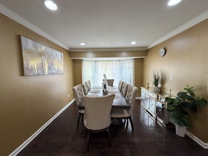 Uma sala de jantar com uma mesa comprida, cadeiras estofadas, um aparador decorativo e um quadro na parede.
