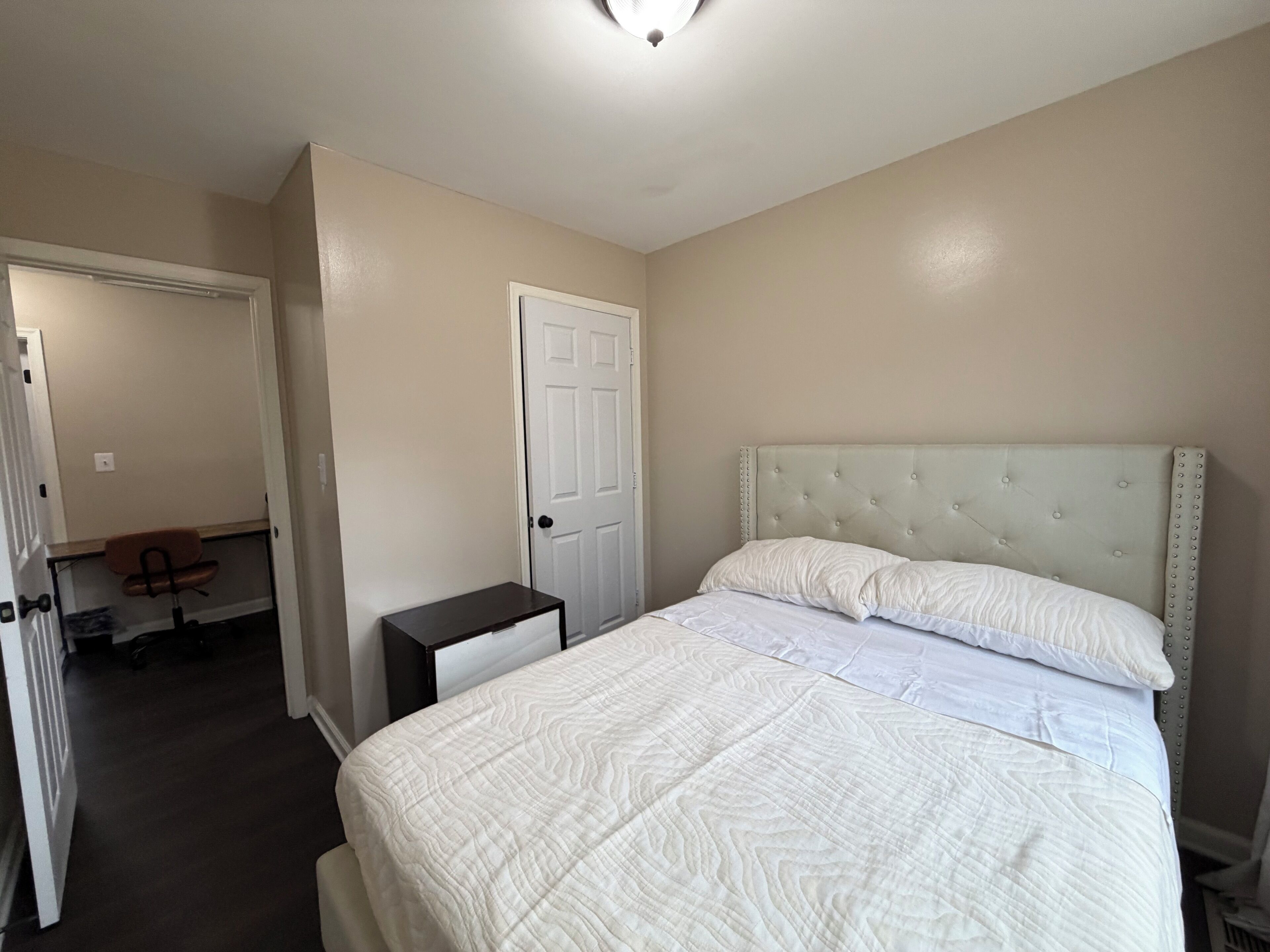 A bedroom with a bed, a nightstand, a chair, and a door.