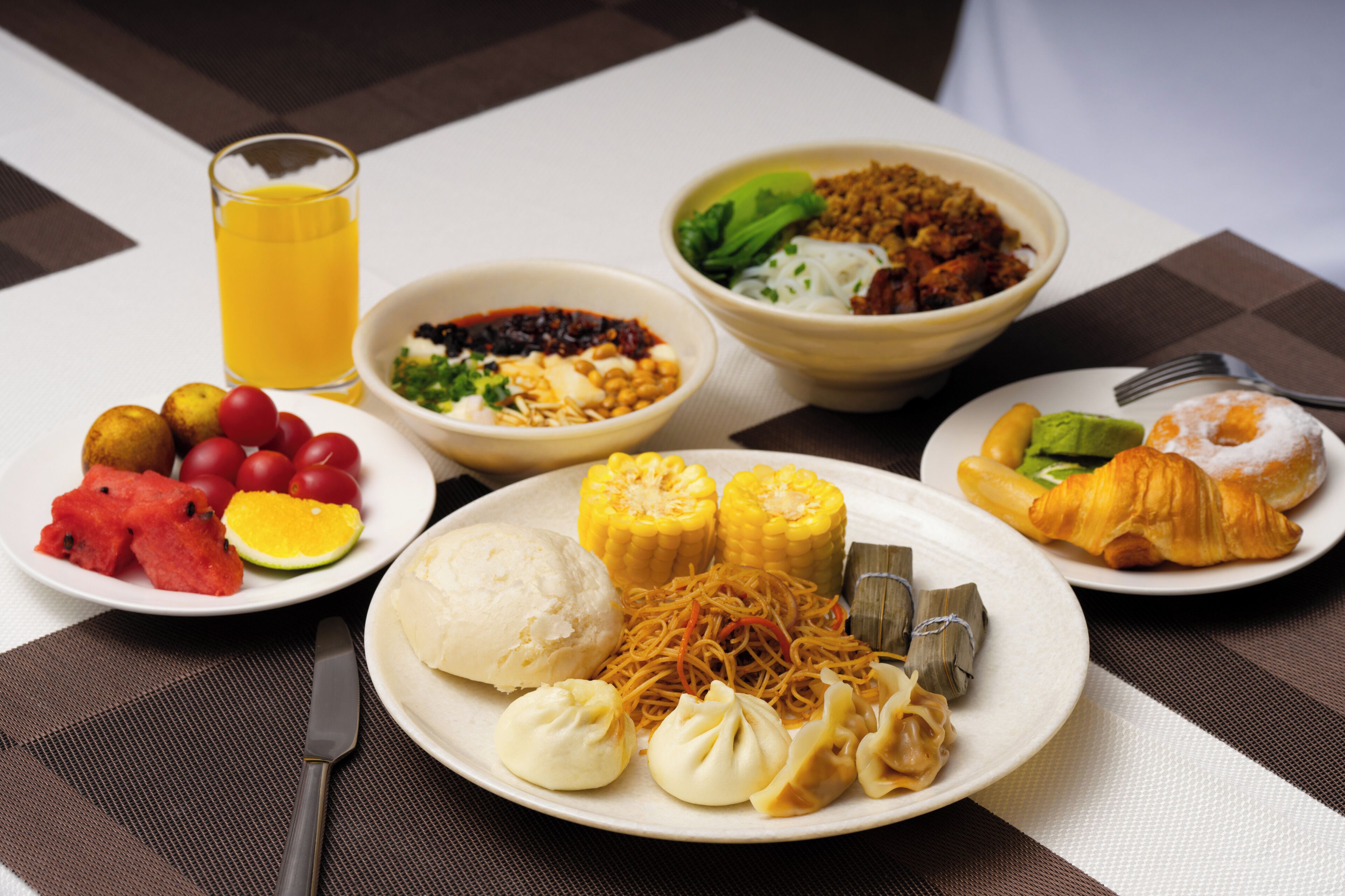 A table with various dishes including corn on the cob, dumplings, and a croissant.