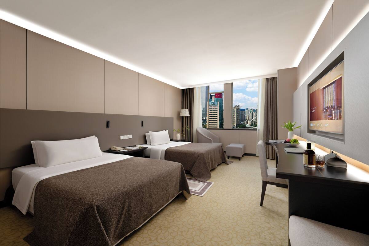 A hotel room with two beds, a desk, a chair, a TV, and a city view.