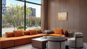 Un salon moderne avec un canapé d’angle, deux fauteuils, une table basse et une vue sur le paysage urbain grâce à de grandes fenêtres.