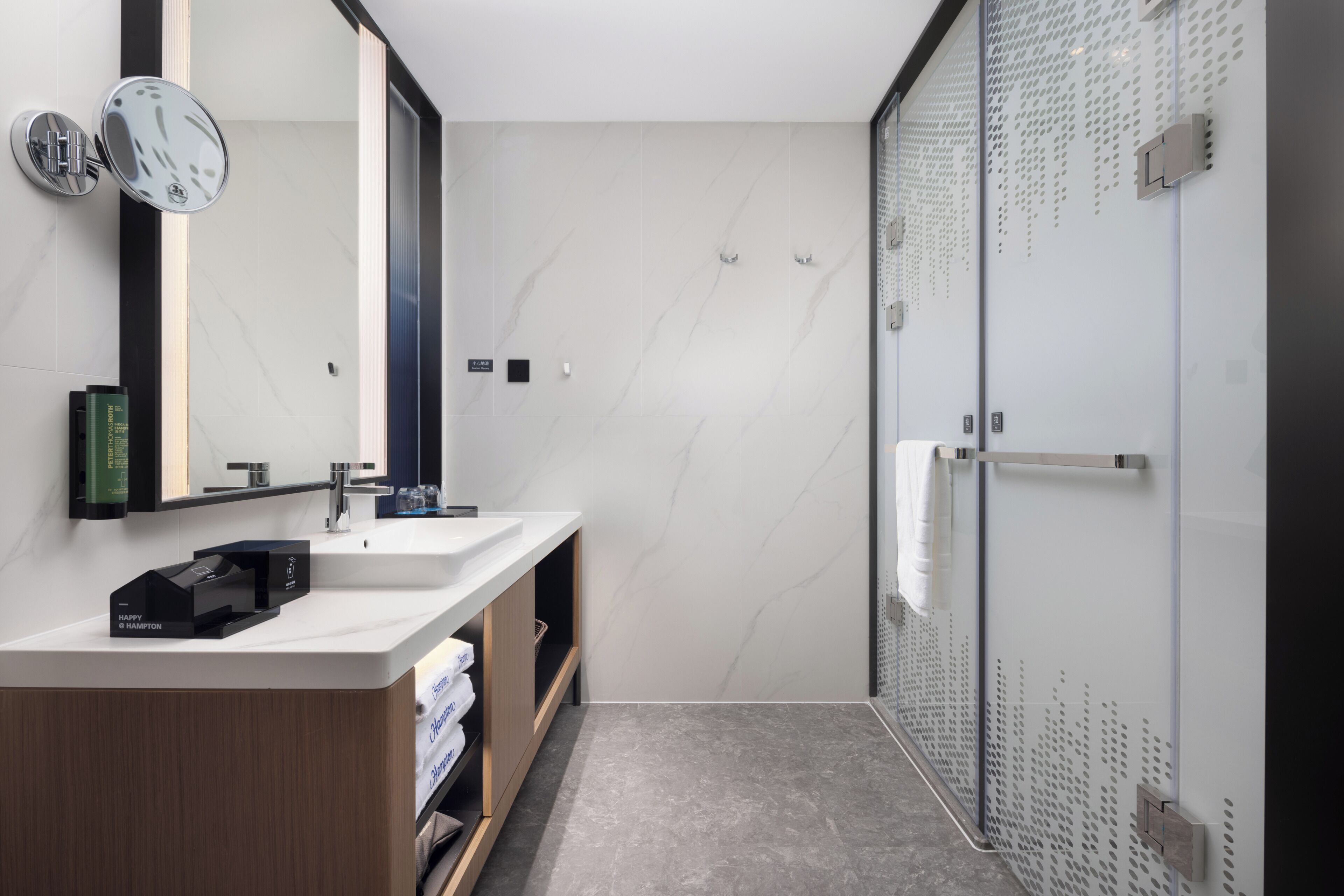 A modern bathroom with a large mirror, two sinks, a shower with a glass door, and a towel rack.