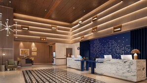 Un hall d’hôtel moderne avec un comptoir d’accueil en marbre, un espace salon et une moquette à motifs.