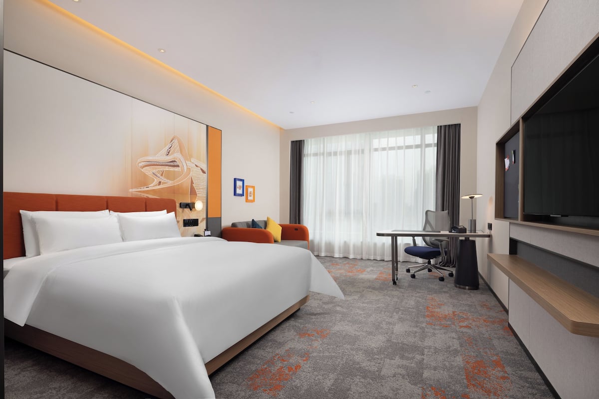A hotel room with a large bed, a desk, a chair, a television, and a window with curtains.