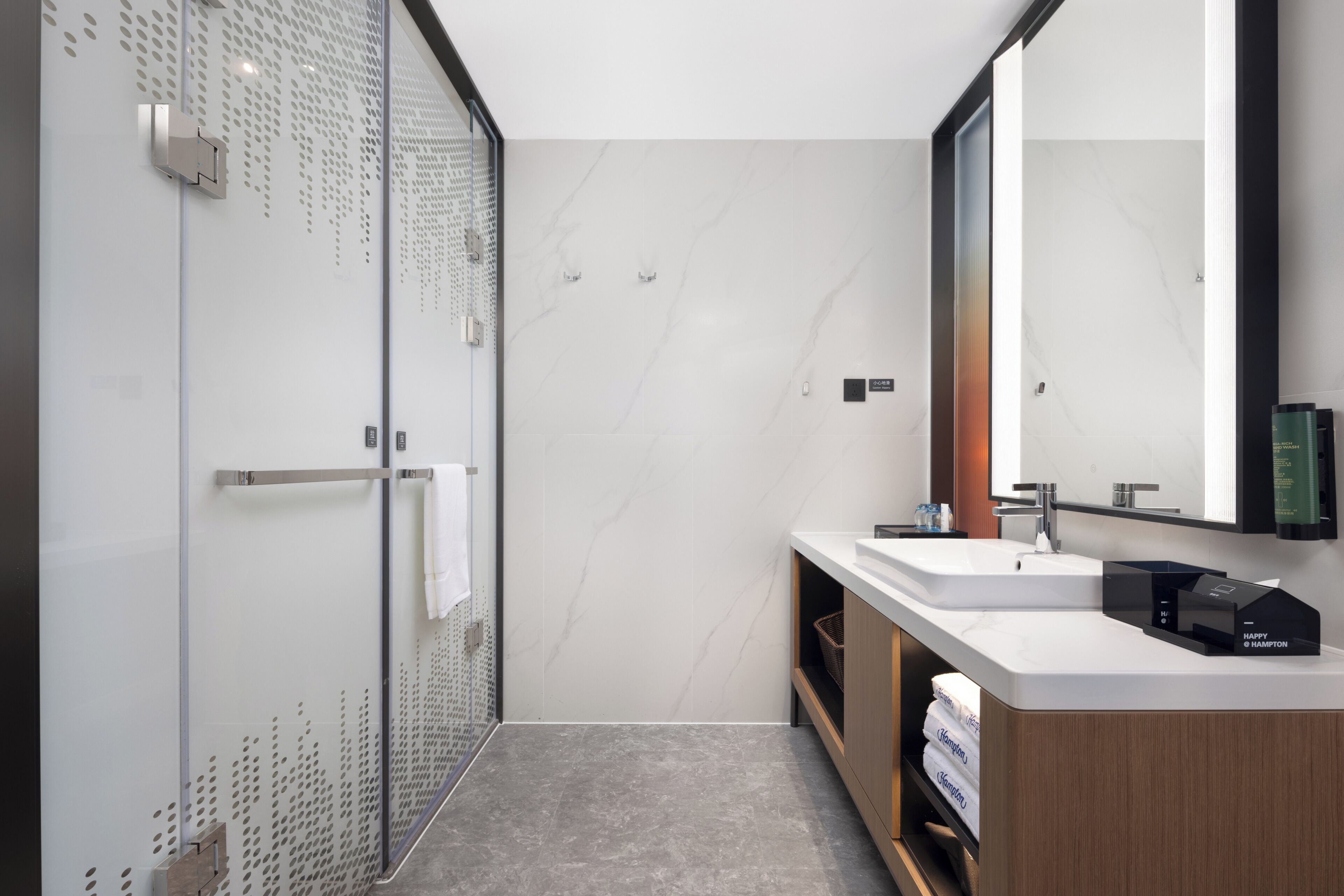 A modern bathroom with a glass shower enclosure, a large mirror, and a wooden vanity with a sink.