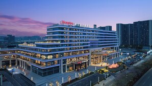 Un hôtel à plusieurs étages, reconnaissable à son grand panneau « Hilton », doté d’un espace d’entrée aménagé et d’un parking.