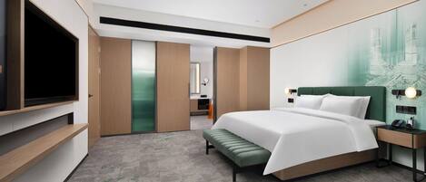 A modern hotel room with a large bed, a television, a desk, and a bathroom visible through a sliding door.
