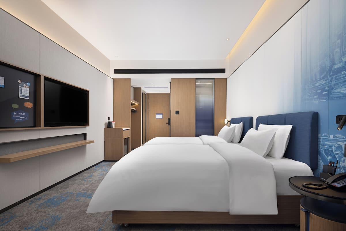A modern hotel room with a large bed, a flat-screen TV, a desk, and a wardrobe.